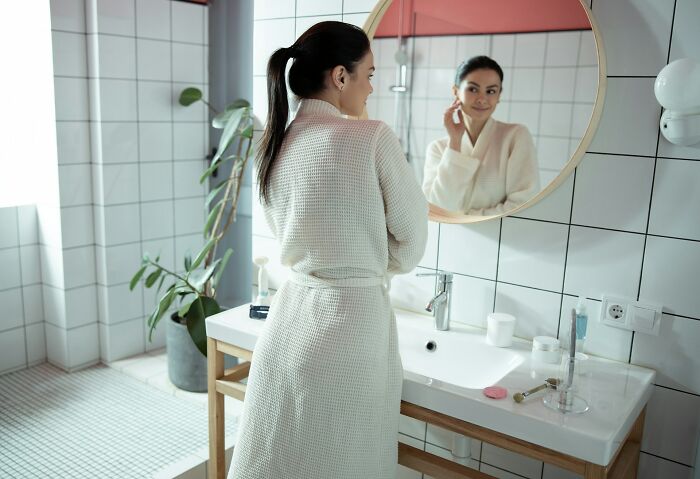 Woman in a white robe looking in the bathroom mirror, reflecting on lessons men learned about women in relationships.