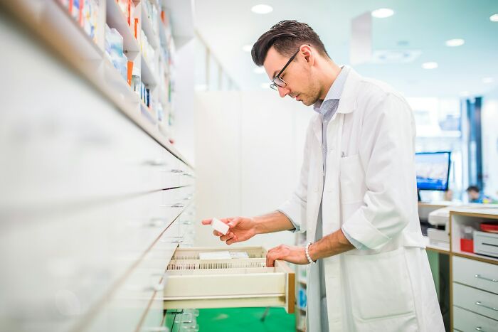 Man in a white lab coat organizing medication in a pharmacy, representing workplace environment and potential scandals.