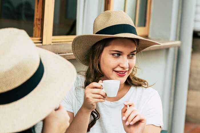 Young woman wearing a hat holding a coffee cup, engaging in conversation about men sharing lessons from serious relationships.