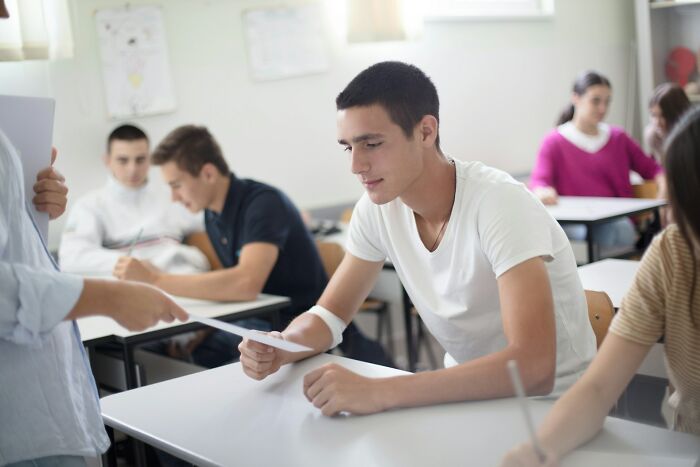 Teenagers sitting in a classroom, focusing on papers, illustrating signs someone is still stuck in their high school era.