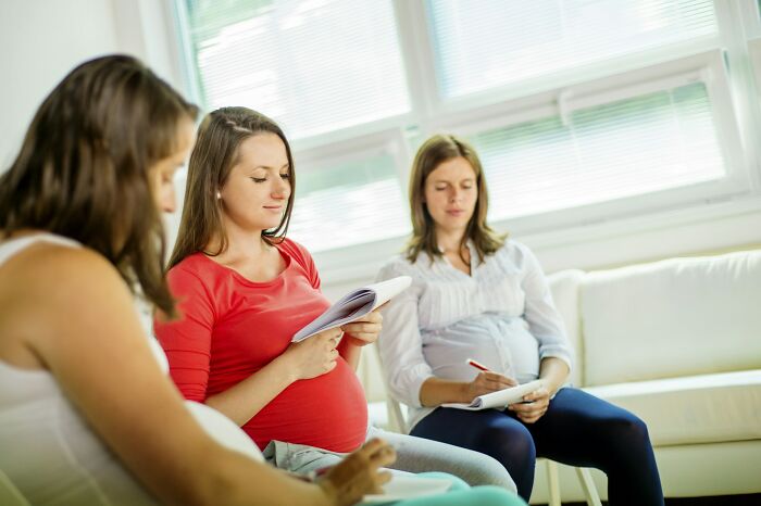 Three pregnant women attending a modern parenting class, taking notes and discussing parenting trends indoors.