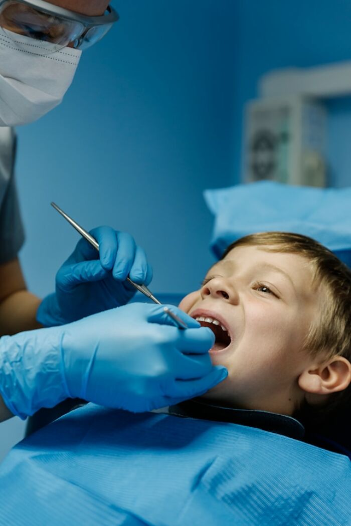 Young boy at dental checkup with dentist wearing gloves and mask performing clever and funny moment in clinic.