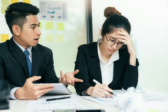 Two professionals discussing harmful habits in an office, showing concern during a stressful work meeting.