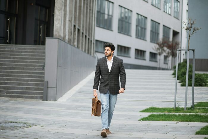 Man walking outdoors in casual blazer and jeans carrying a briefcase, illustrating everyday things people accidentally did wrong.