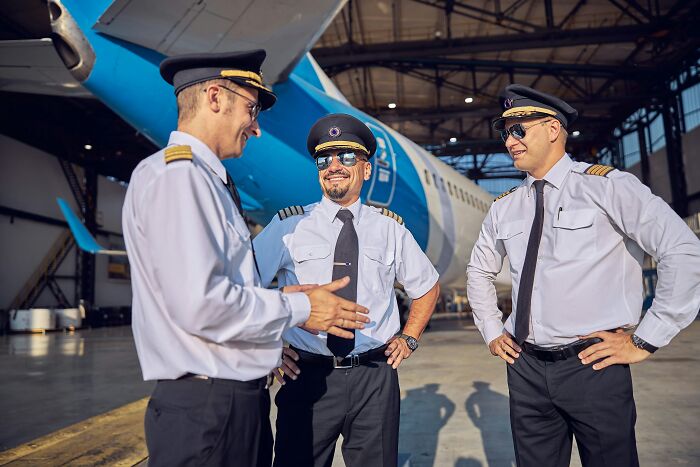 Three pilots in uniform standing and talking in an airplane hangar revealing dark, dirty truths about their industry.