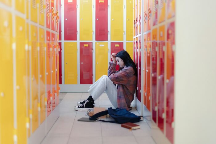Teen girl sitting on school floor by colorful lockers, symbolizing signs someone is stuck in their high school era years later.