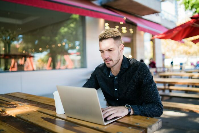 Man working on laptop at outdoor cafe, illustrating the hidden realities of a digital nomad’s life beyond Instagram.