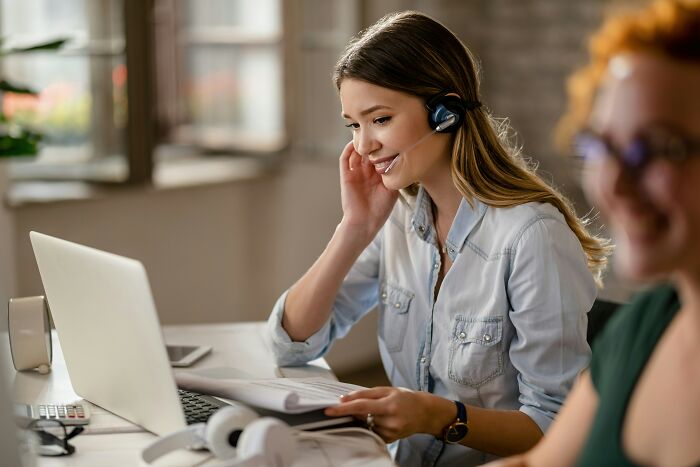 Young female employee wearing a headset working on laptop, representing employees revealing industry truths at office.