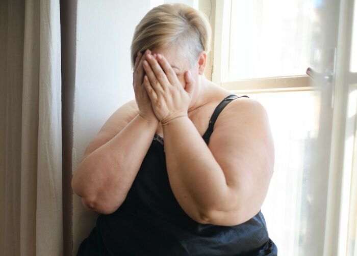 Woman covering her face while sitting by a window, expressing grief and emotion related to unexpected funeral moments.
