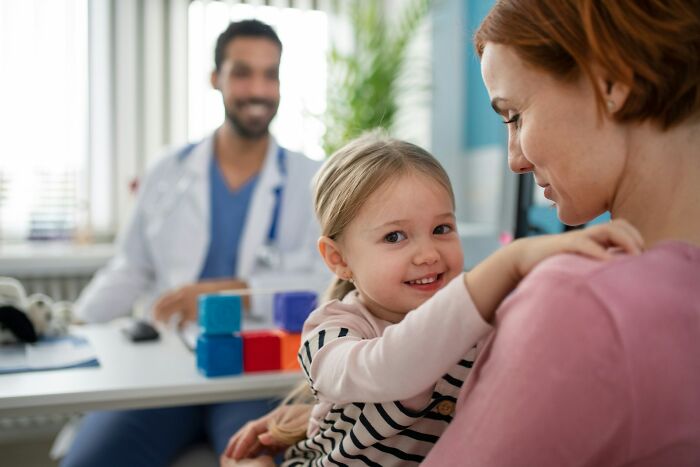 Young child with mother smiling in a doctor’s office while ER staff discuss challenges patients create in their job.