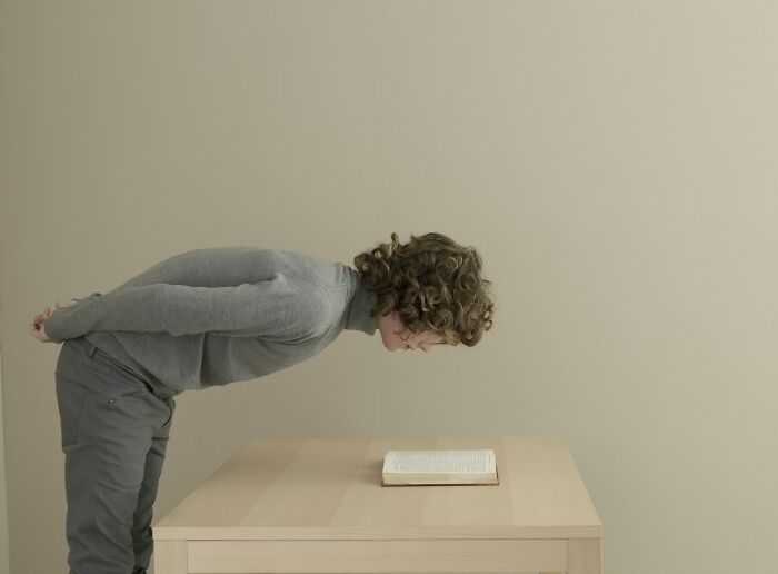 Person with curly hair wearing a gray sweater leaning forward to closely observe an open book on a table about toxic habits.