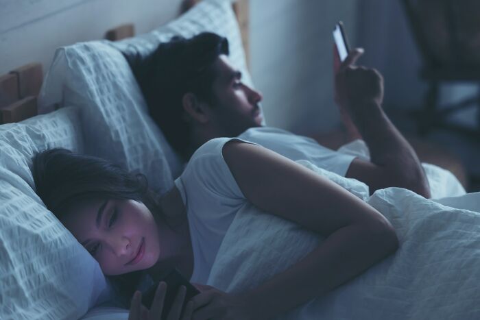 Couple in bed looking at phones, highlighting secrets and dark secrets impacting how people see each other.