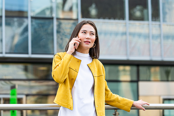Woman talking on phone outside modern building, looking concerned about HOA fine for festive Christmas decor Woman talking on phone outside modern building, looking concerned about HOA fine for festive Christmas decor