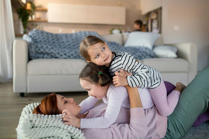 Mother playing on the floor with her two daughters, illustrating signs of someone stuck in their high school era years later.