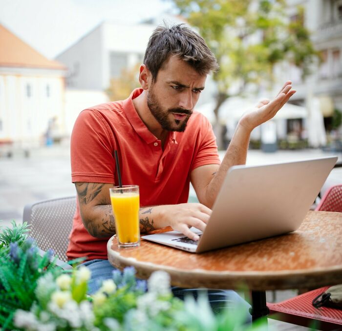 Man in a red shirt working on a laptop outdoors, showing the challenging side of a digital nomad’s life.