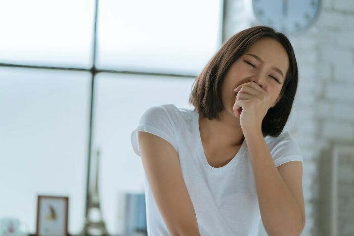 Young woman in white shirt covering mouth while laughing, illustrating challenges ER staff face with difficult patients