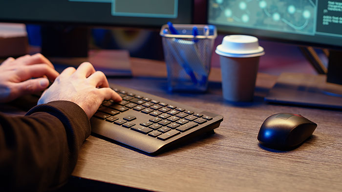 Man typing on a spare keyboard at a desk with a coffee cup and computer mouse, highlighting keyboard lending gesture.
