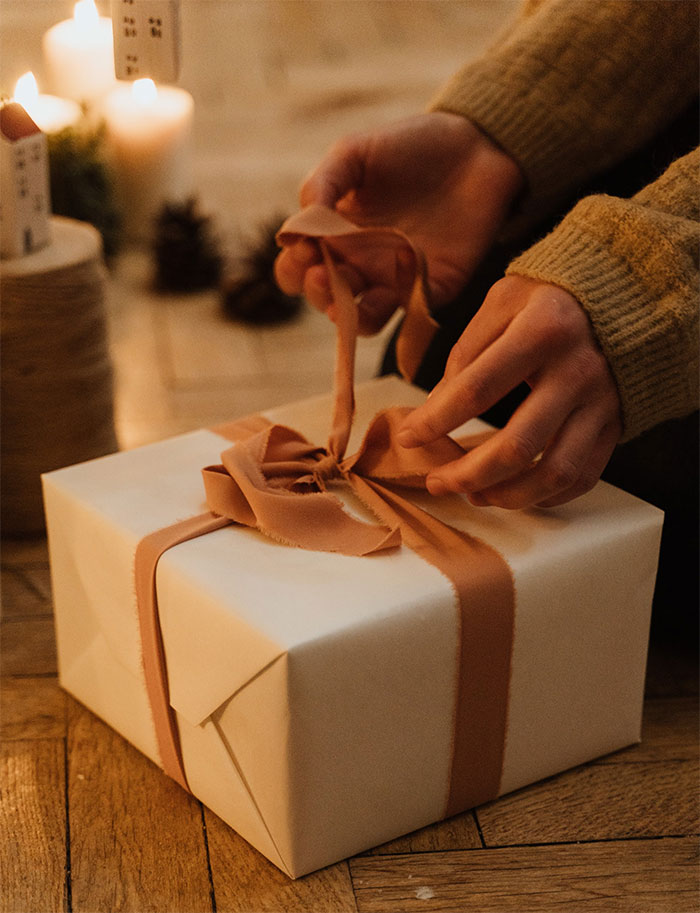 Hands untying a Christmas gift box with ribbon in a cozy setting, relating to unthoughtful gift and relationship issues.
