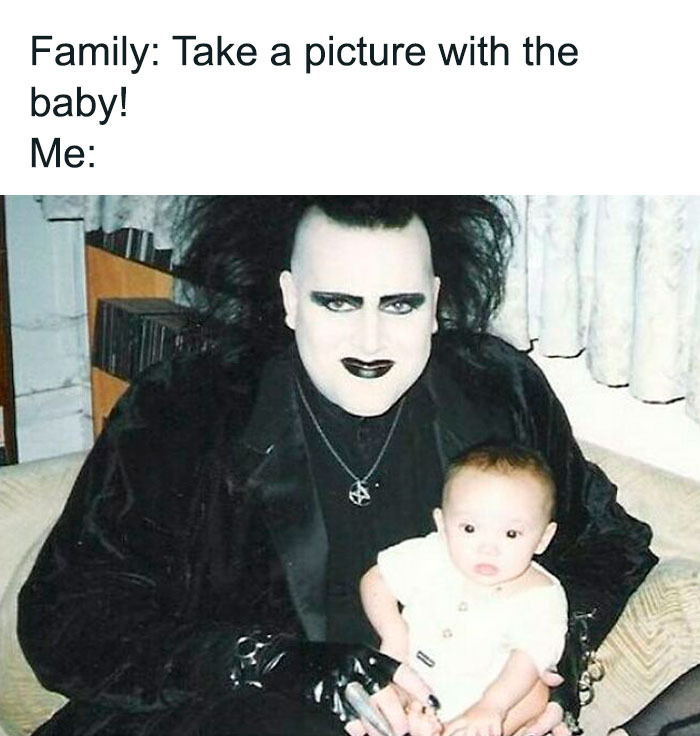 Person in goth makeup and clothing holds baby, contrasting gothic style with family photo setting, highlighting goth memes.