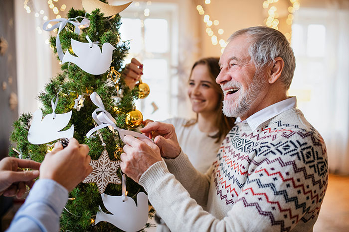 Grandpa and granddaughter decorating Christmas tree together, smiling and enjoying festive holiday moments indoors.