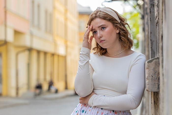 Young woman leaning against wall looking upset, reflecting on family issues and feeling emotionally hurt.