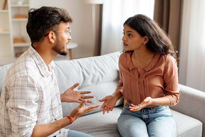 Young man and woman having a tense conversation on a couch, highlighting conflict in family relationships.