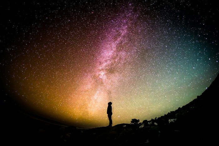 Silhouette of a person standing under a vivid starry sky, representing mysteries we aren’t getting closer to solving.