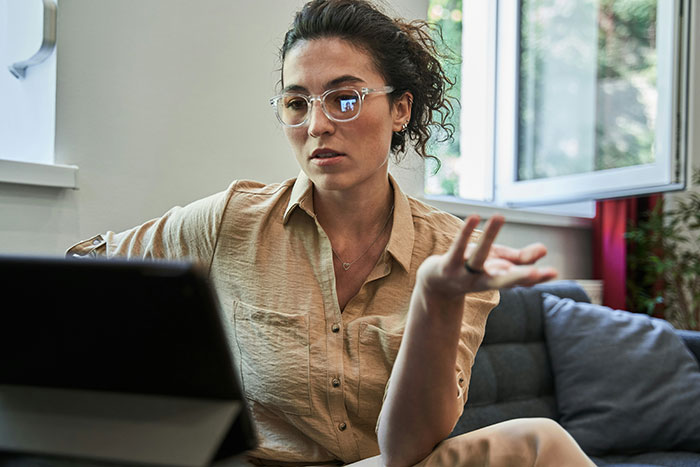 Woman in glasses speaking seriously on a digital device during a private therapy session recording concern discussion.