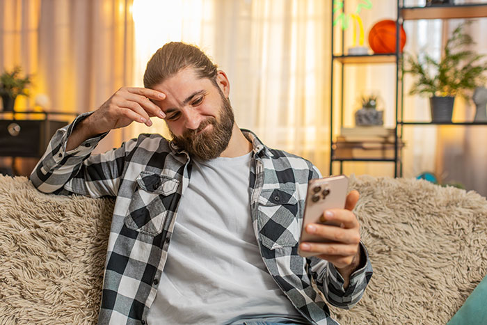Man in a plaid shirt holding phone, appearing concerned, depicting guy recording wife’s private therapy sessions out of concern.