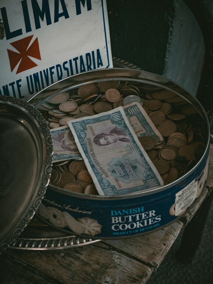 Vintage tin of Danish butter cookies filled with coins and banknotes, illustrating disturbing truths about hidden money.