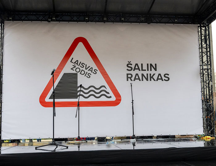 Outdoor stage with microphones and a banner featuring a protest sign related to Lithuania lawmaker&rsquo;s cat consent.