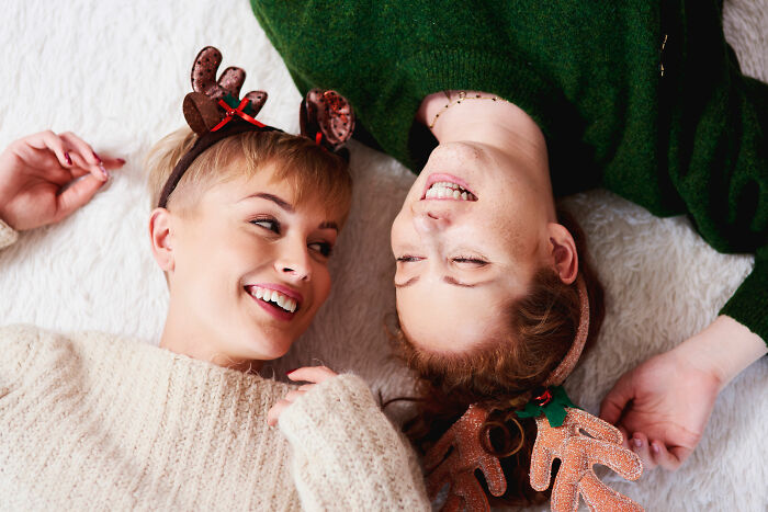 Two women wearing holiday reindeer headbands lying down smiling, relating to partner holiday gift relationship insights.