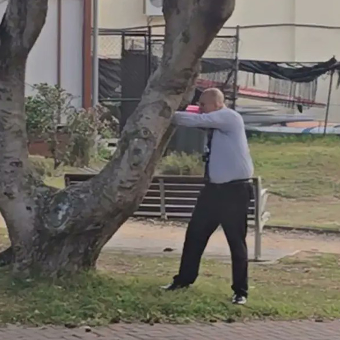 Man in a white shirt and black pants performing a defensive move near a tree, Bondi Beach attacker incident.