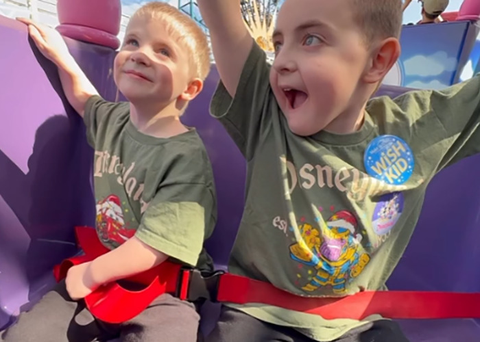 Two young boys wearing matching Disney shirts enjoying a ride, linked to terminally ill kids and Hilary Swank apology news.