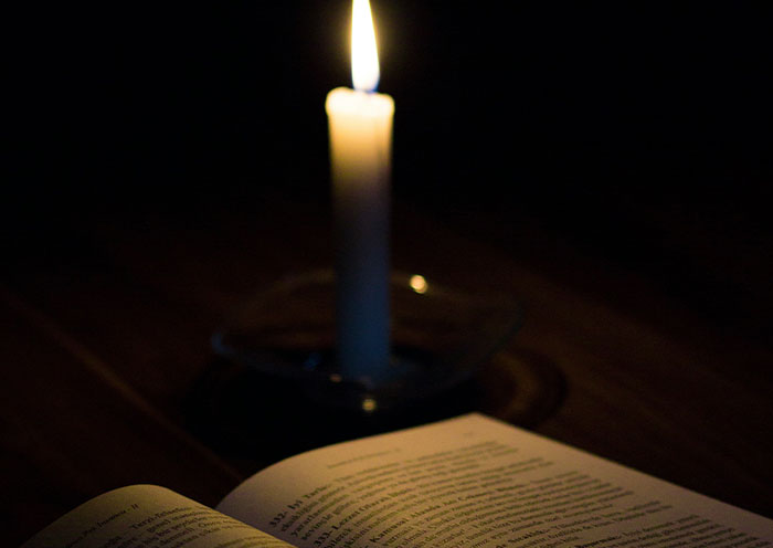 An open book illuminated by candlelight in a dark room, evoking the mood of learning bizarre facts from history.