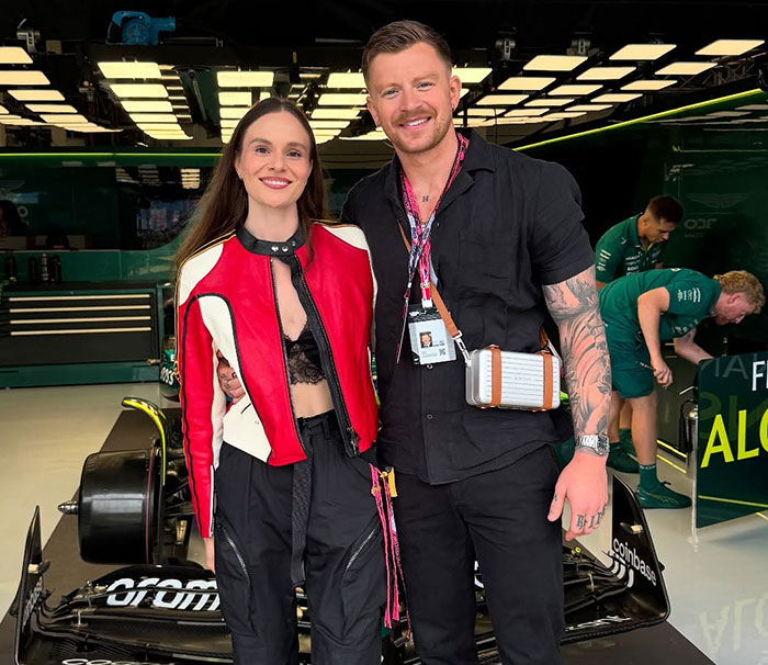 Adam Peaty and partner smiling together near a racing car, linked to Gordon Ramsay wedding speech and family drama.