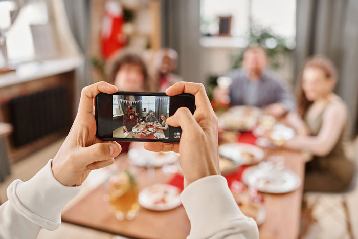 Hands holding a smartphone capturing family pictures, highlighting a woman excluded by homophobic MIL in the photo.