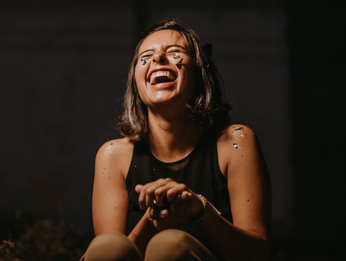 Young woman with confetti on her face and arms laughing joyfully in a dark setting after terrible family photo exclusion.