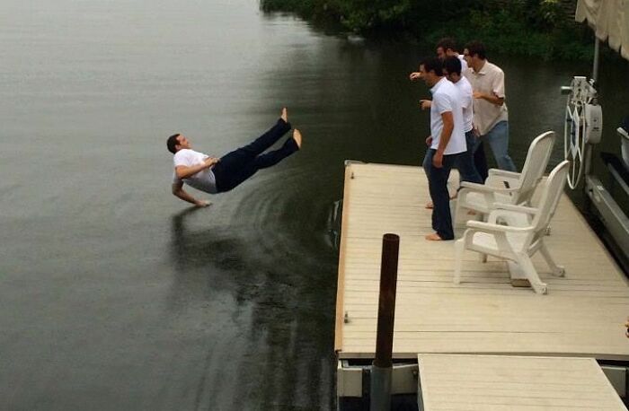 Man captured mid-air falling backward into water, with friends on a dock watching in this funny perfect timing pic.