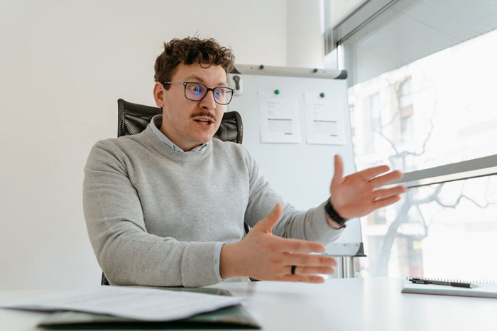 Man in gray sweater explaining open marriage issues with expressive hand gestures in a bright office setting. Man in gray sweater explaining open marriage issues with expressive hand gestures in a bright office setting.