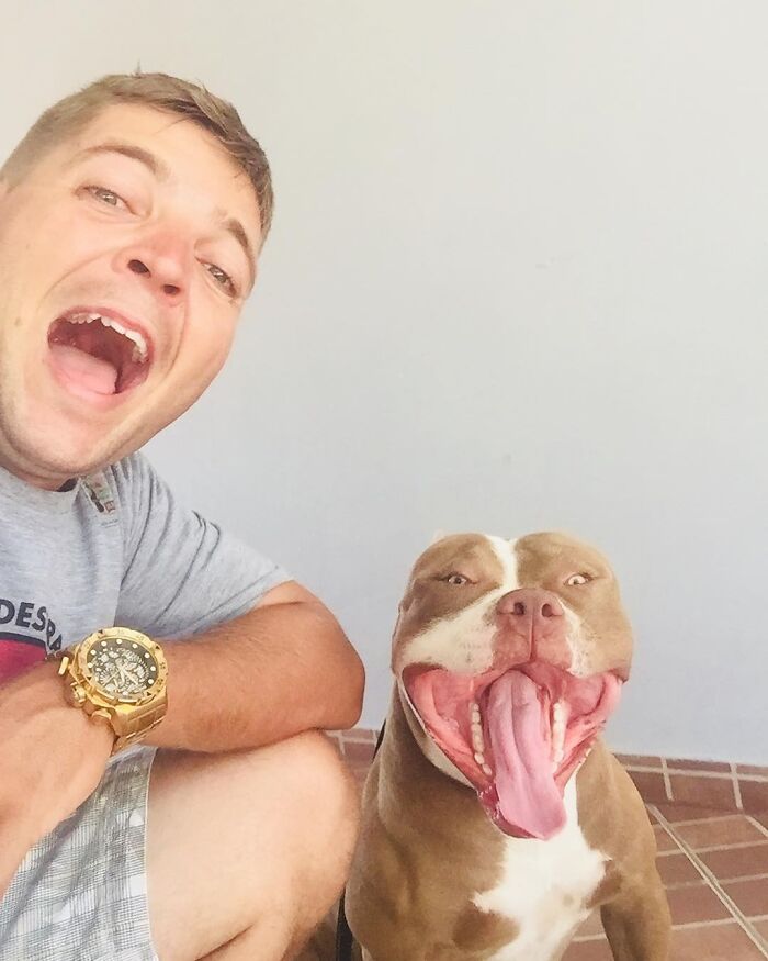 Man with a large watch happily posing next to a brown and white dog with tongue out and a joyful expression.