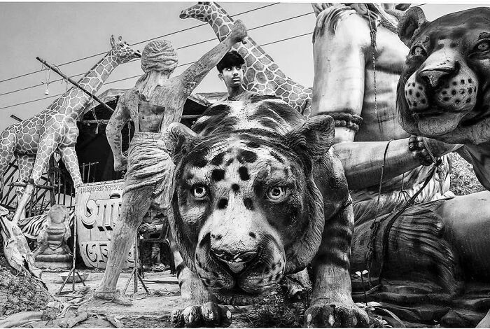 Black and white photo of large animal sculptures including a tiger and giraffes with a person working among the statues.