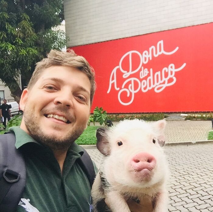 Man smiling outdoors holding a piglet, unrelated to a wild vulture bonded with a human, dog with wings concept.