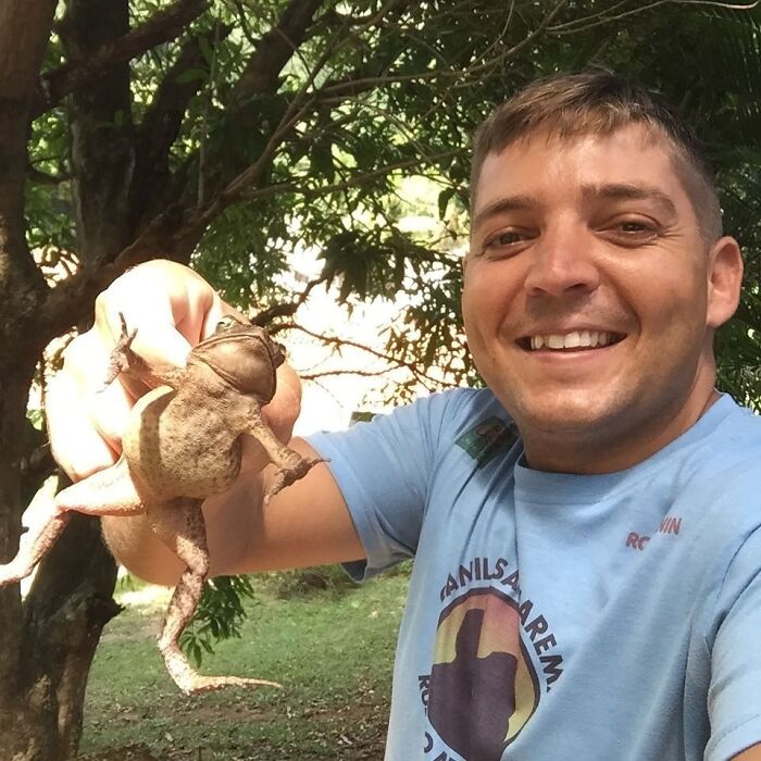 Man smiling outdoors holding a toad, unrelated to wild vulture bonding with a human or dog with wings theme.