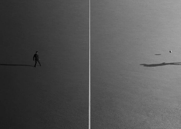 Minimalist black and white photo of a solitary person near a white line, showcasing striking minimalism in photography art.