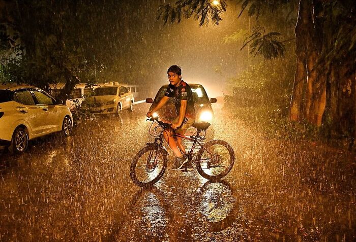 Boy riding a bicycle in heavy rain on a street in Mumbai, capturing everyday life in vibrant city scenes.