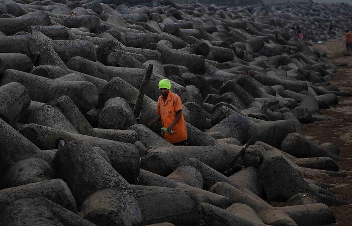 Worker in a bright orange shirt and green cap among concrete tetrapods capturing everyday life in Mumbai street scenes.