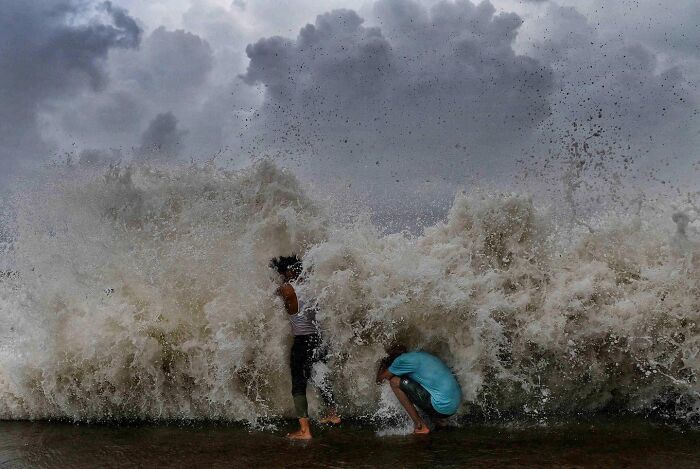 Two boys playing near large waves crashing on the shore, capturing everyday life in Mumbai street scenes.