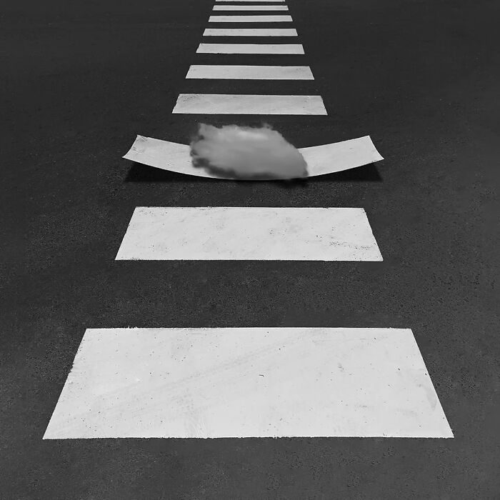 Crosswalk lines on asphalt with one line bent upward and a small cloud underneath, showcasing minimalism photography art.