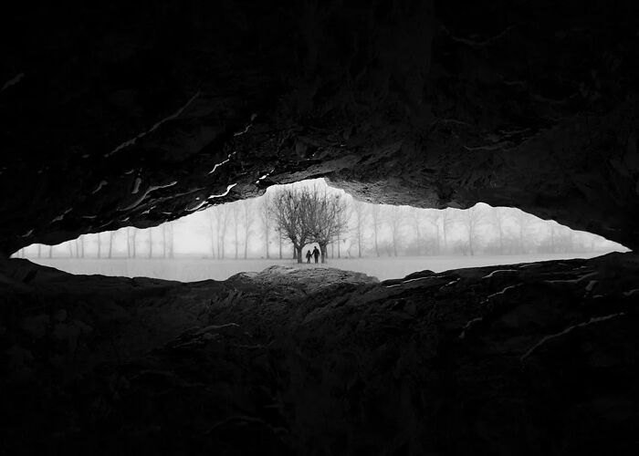 Black and white minimalism photograph of two people standing near a tree, framed by a cave opening turning minimalism into art.